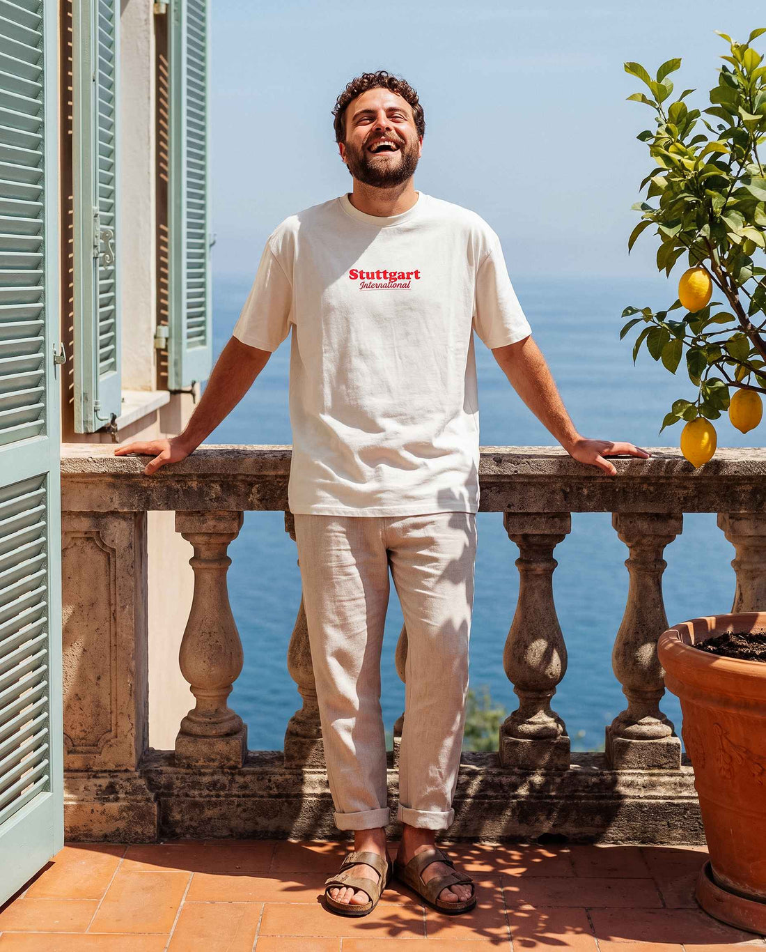 Mann mit Stuttgart Shirt "International" steht seitlich zur Kamera und schaut in die Kamera. Hinter ihm das Meer.