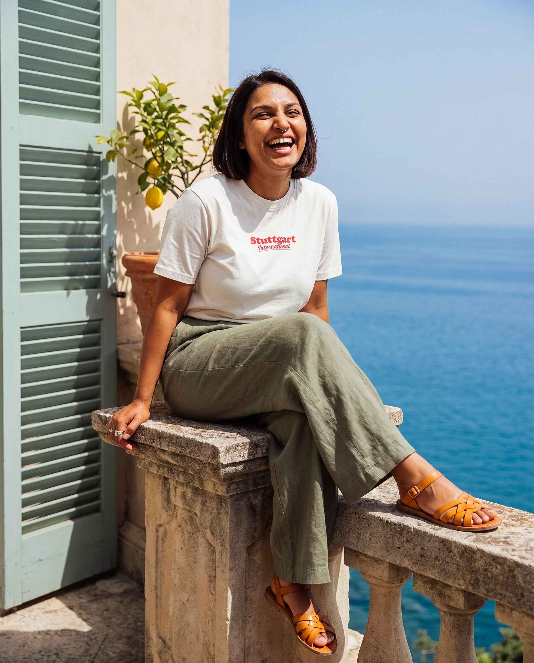 Frau sitzt auf Steinbalustrade mit Stuttgart Shirt "International" und lacht dabei authentisch.